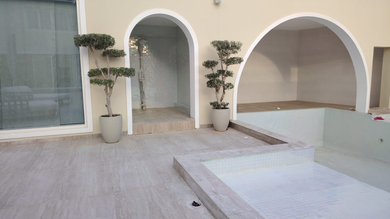 Modern indoor pool area with arched doorways and potted plants.