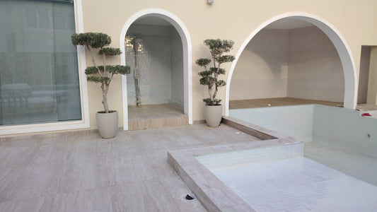 Modern indoor pool area with arched doorways and potted plants.